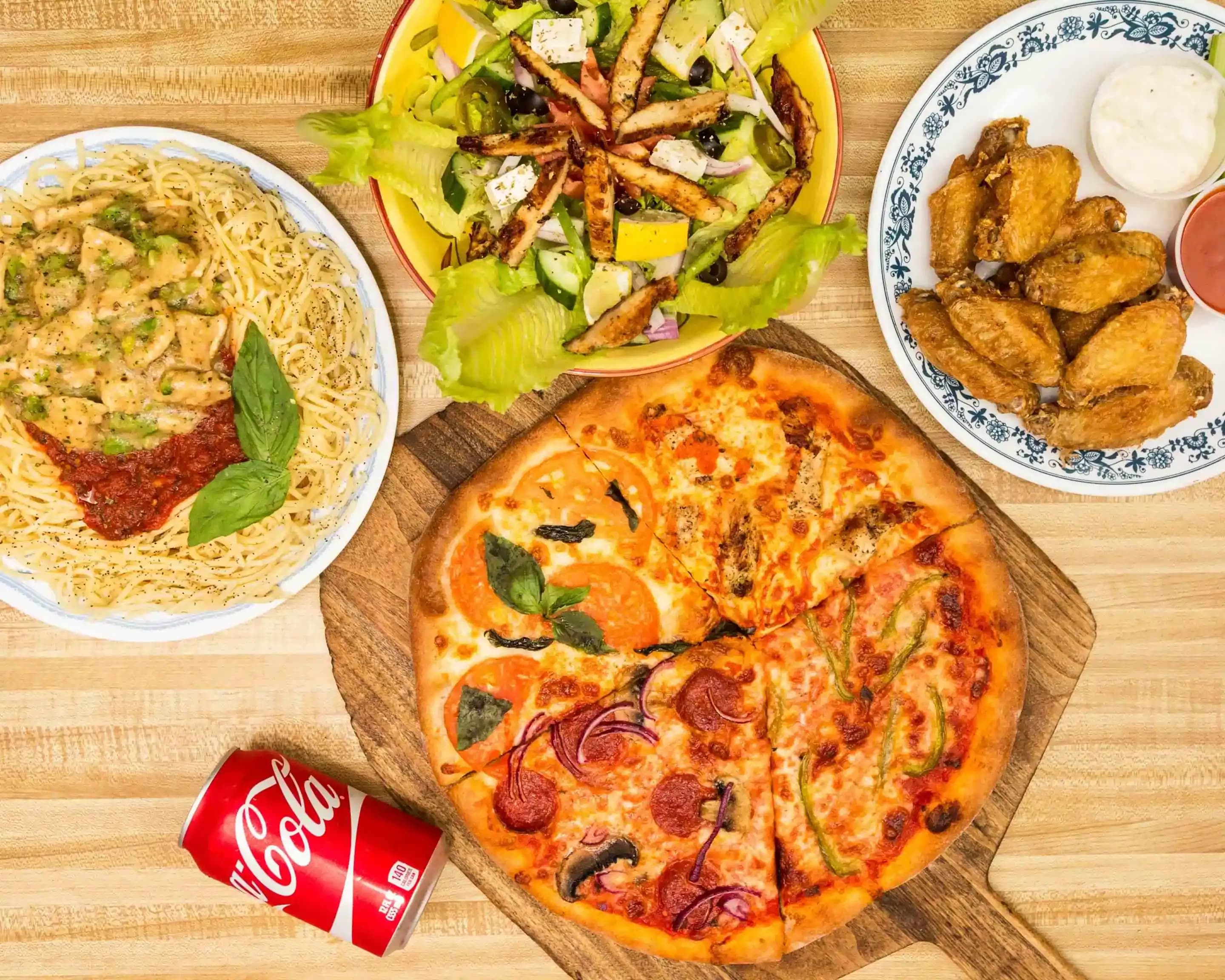 Et bord fyldt med pizza, pasta, kyllingevinger og calzones