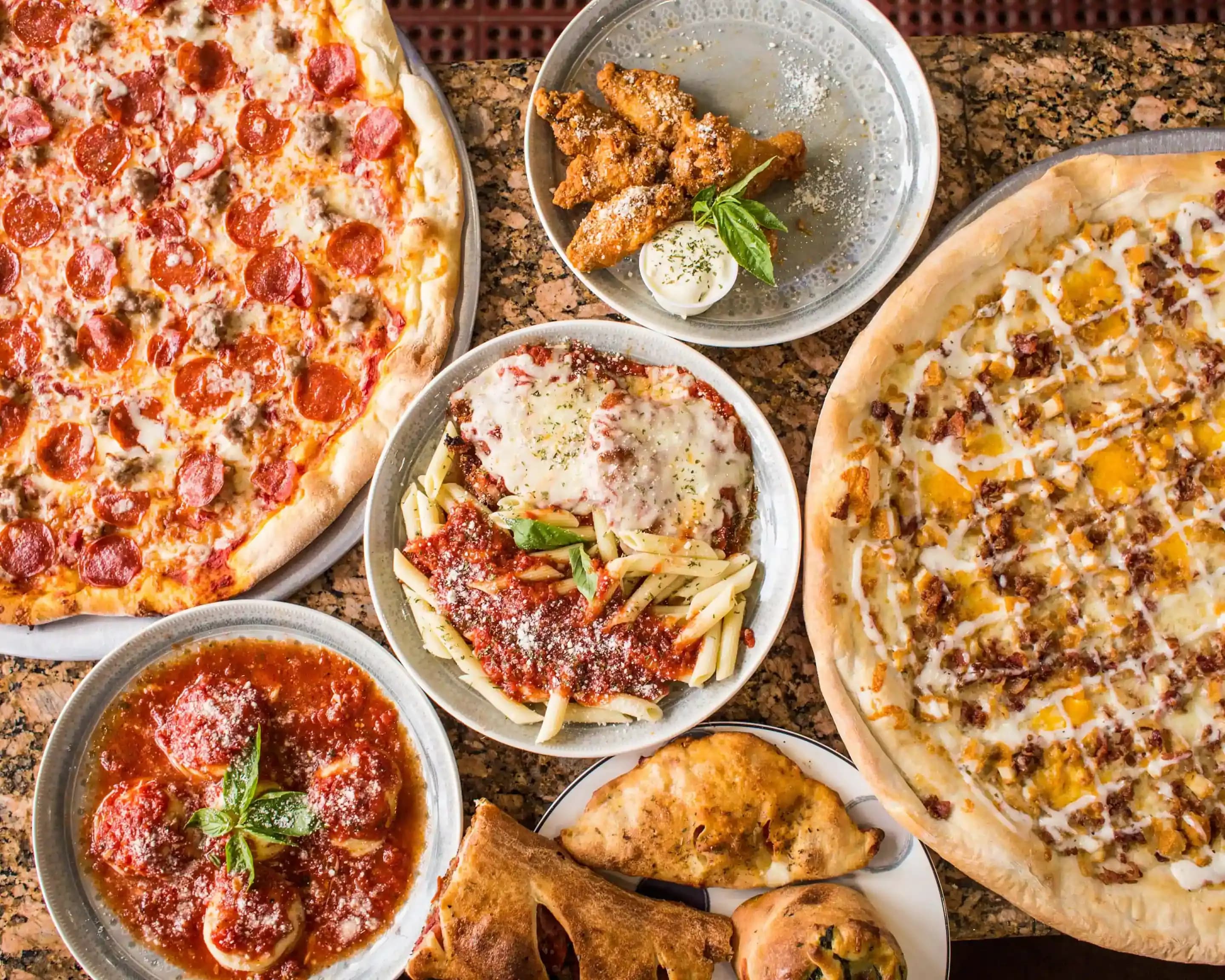 Bordmåltid med pizza, pasta, salat og kyllingevinger